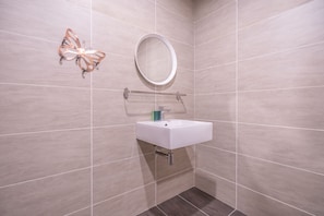 Un baño con un lavamanos blanco, un espejo redondo y una decoración con forma de mariposa en la pared.
