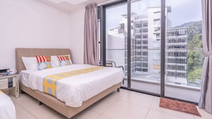 A modern hotel room with a large bed, a nightstand, a window with a view of buildings and greenery, and a sliding glass door. - OYOHome 89448 Extraordinary Studio (Genting Highlands)