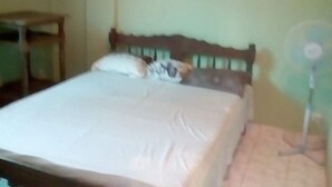 A bed with a wooden headboard, a white bedspread, and a pillow. - Apartment F2 secure city center (Antisiranana)