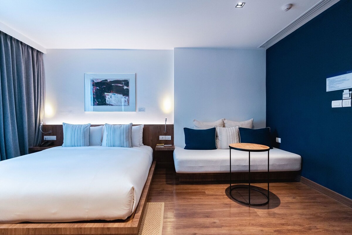 Une chambre d’hôtel avec un grand lit, un petit canapé, une table ronde et une œuvre d’art accrochée au mur.