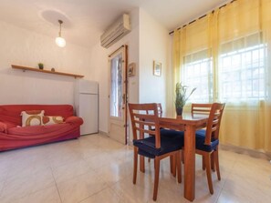 A living room with a red sofa, a dining table with four chairs, a small refrigerator, and a potted plant.