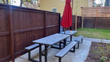 Un patio con mesas de picnic y un paraguas rojo.