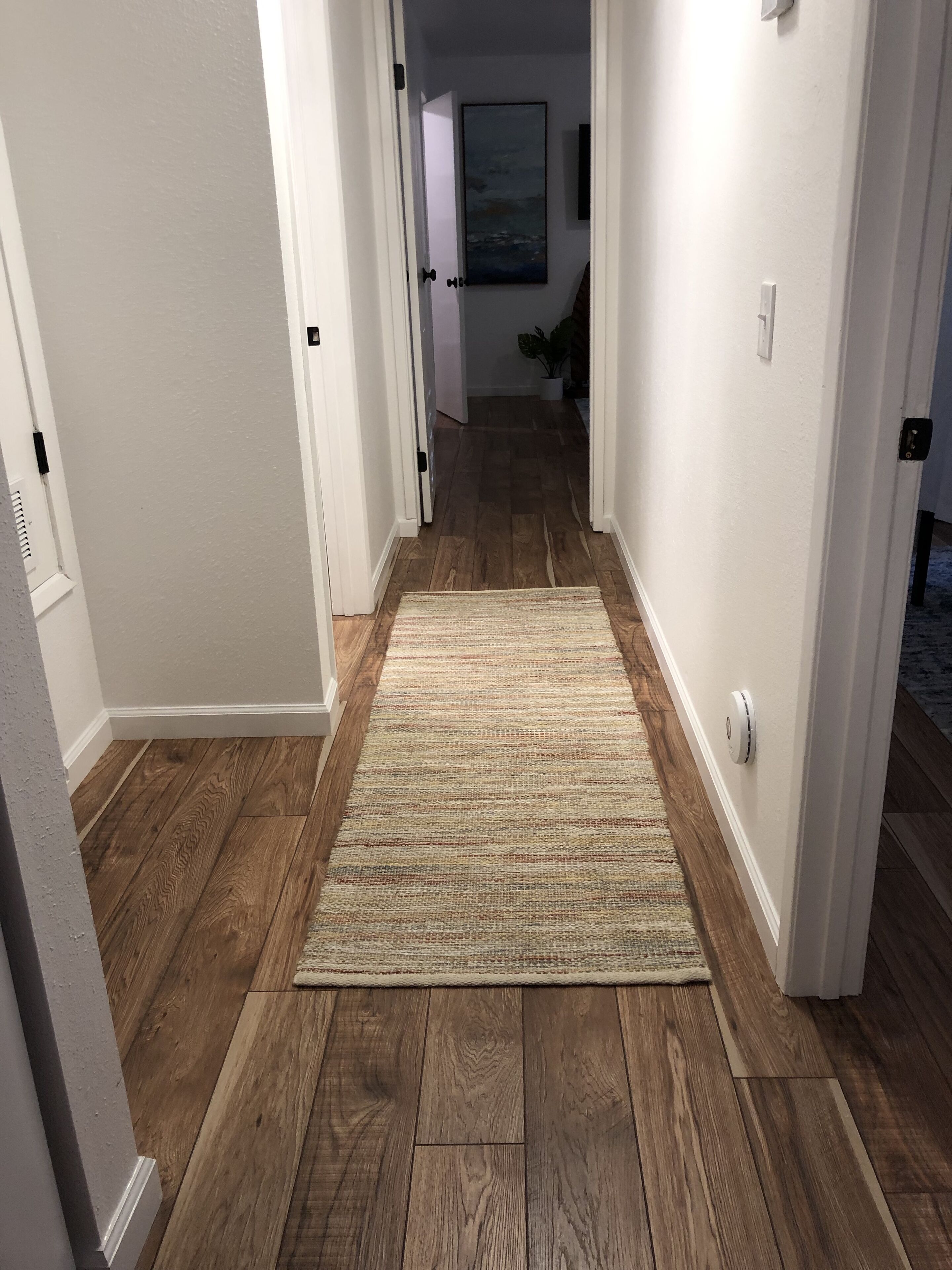 Un pasillo con piso de madera y un tapete color crema.