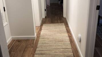 Un pasillo con piso de madera y un tapete color crema.