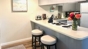 Une cuisine moderne avec un plan de travail blanc, deux tabourets de bar, un grille-pain, une cuisinière et un vase rempli de fleurs.