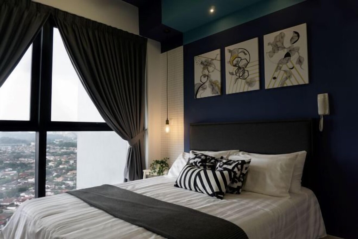 A hotel room with a large bed, a view of the city, and three abstract art pieces on the wall.
