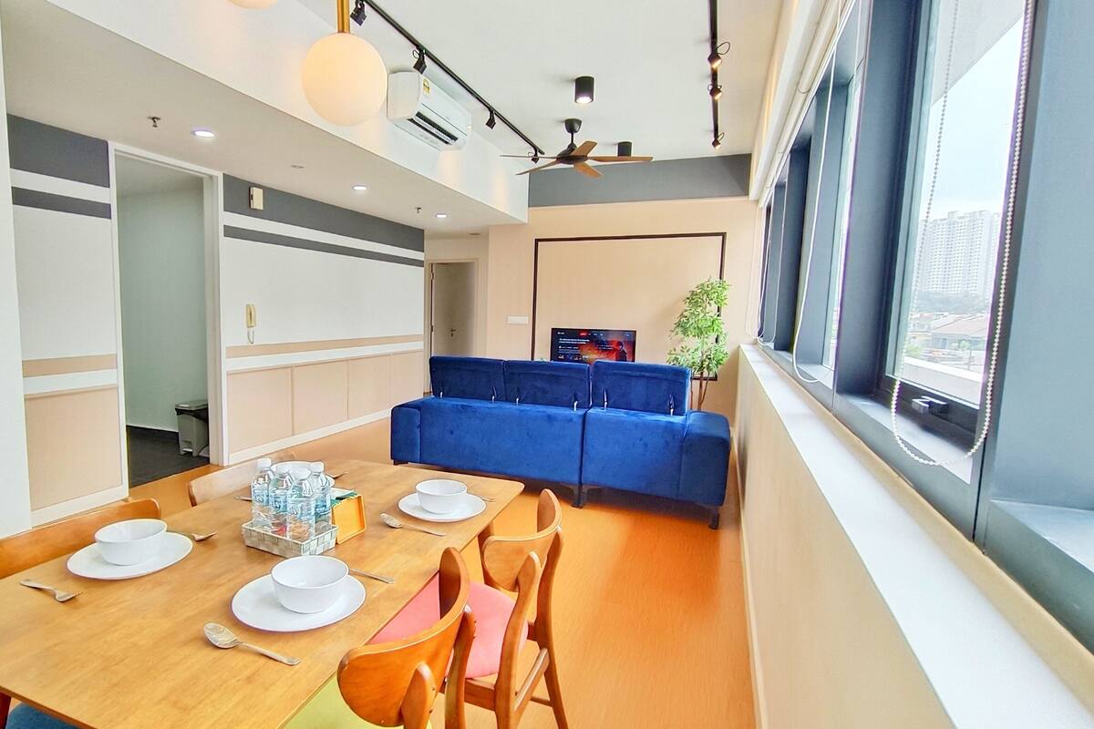 Un espace repas moderne avec une table en bois dressée pour quatre personnes, un canapé bleu et une grande fenêtre offrant une belle vue.