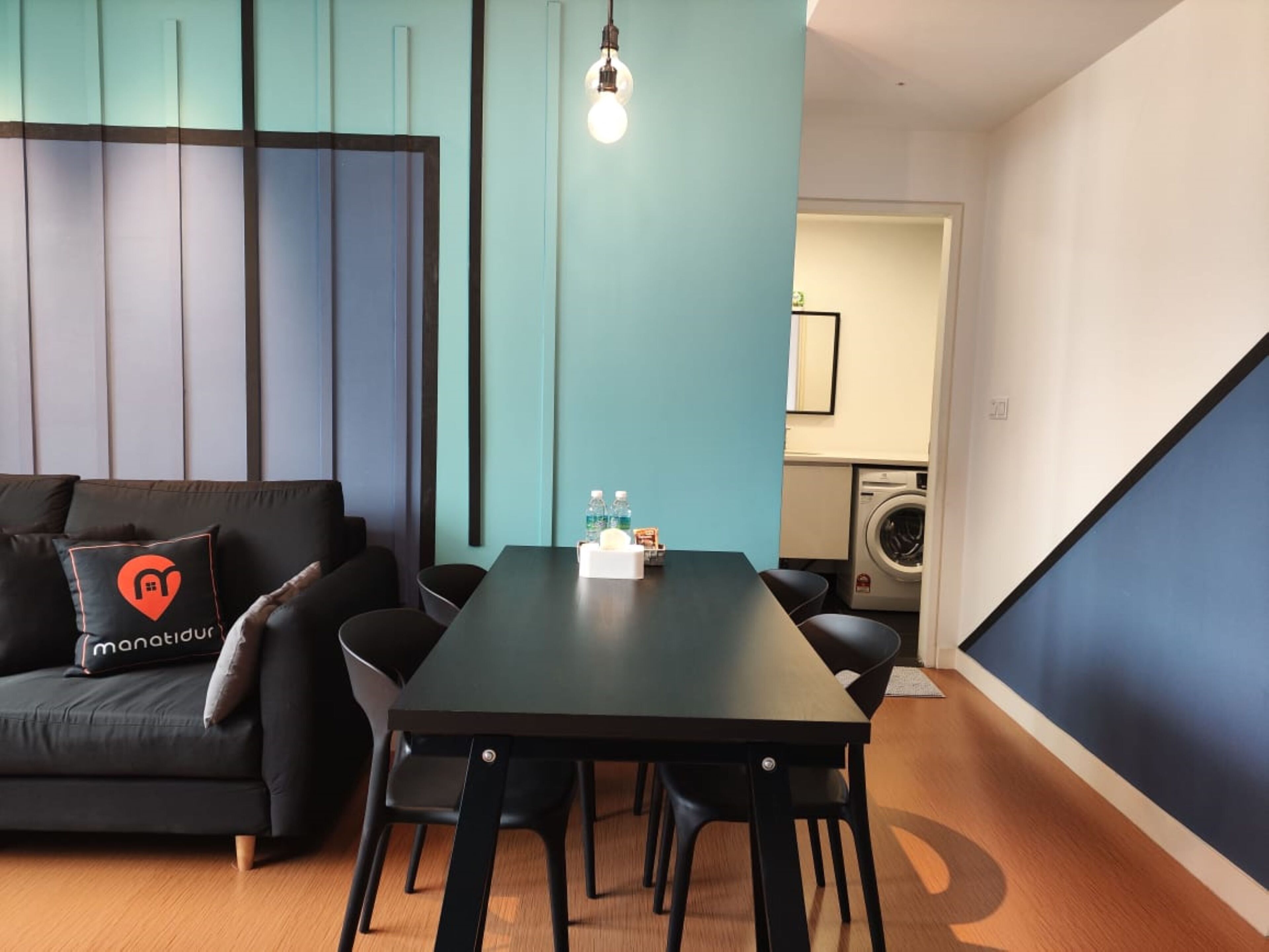 Un salon moderne avec un canapé foncé, une table à manger noire et un mur d’accent bleu.