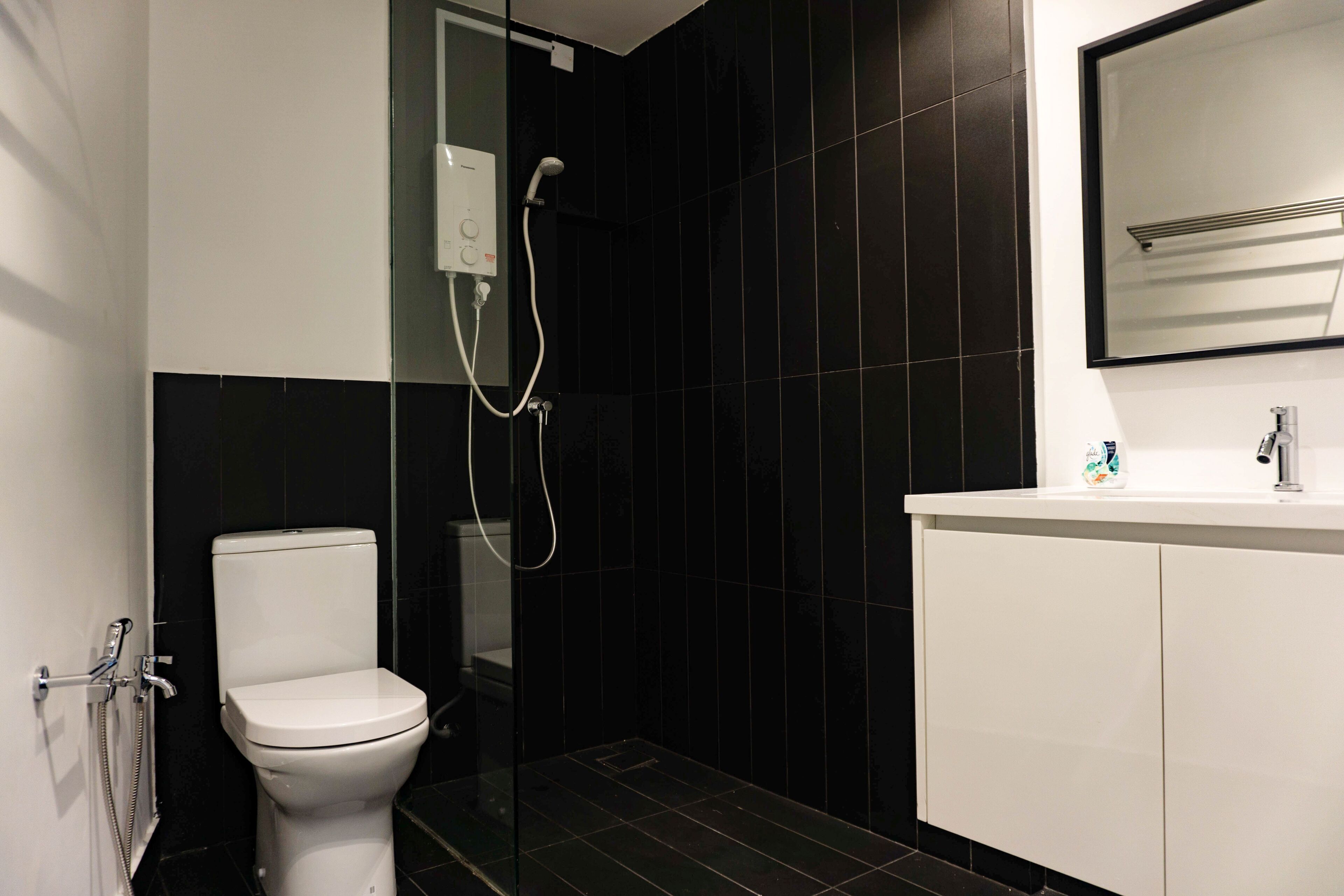 A modern bathroom with a toilet, a glass-enclosed shower, and a white sink with a mirror above it.