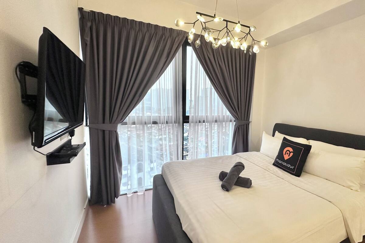 Une chambre d’hôtel avec un lit, un téléviseur fixé au mur et une fenêtre avec des rideaux.