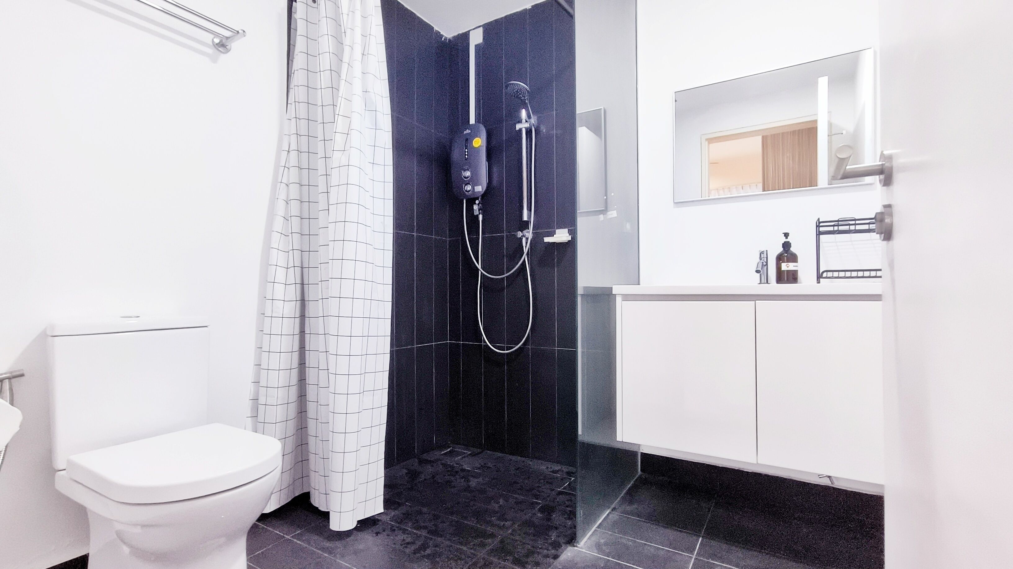 Une salle de bain moderne avec des toilettes blanches, une douche avec un mur recouvert de carreaux noirs et un lavabo blanc avec un miroir au-dessus.