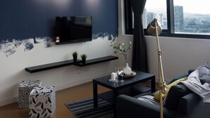 A modern living room with a flat-screen TV mounted on the wall, a black sofa, a coffee table, and a floor lamp.