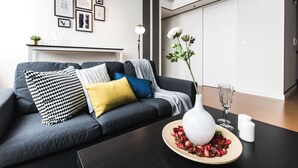 A modern living room with a dark grey sofa, a white vase with dried flowers, and a small table with a wine glass.