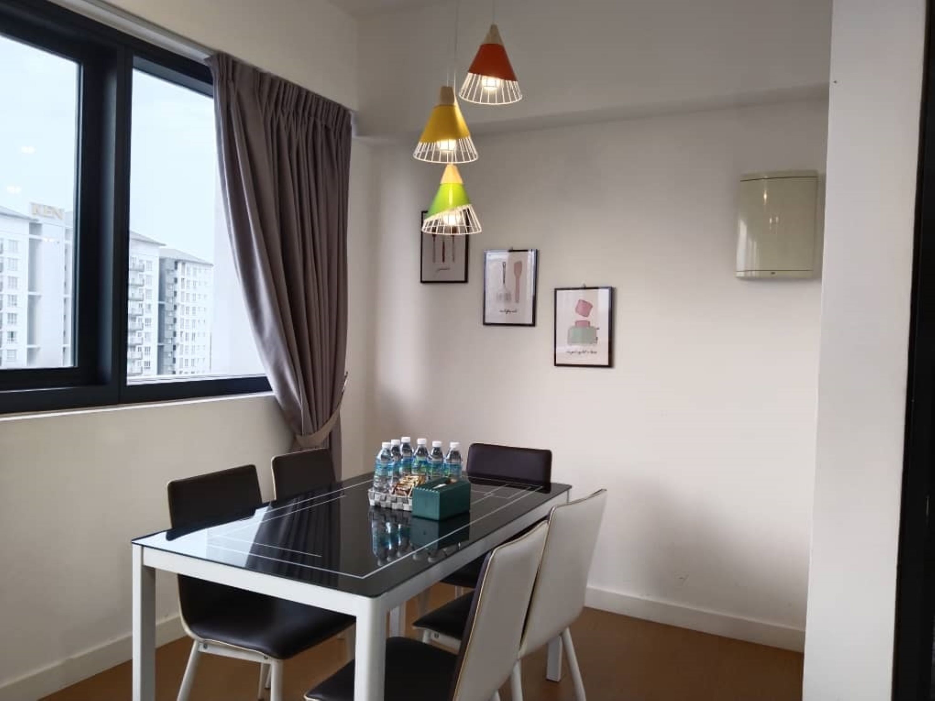A modern dining area with a glass table, white chairs, a water dispenser, and a city view through large windows.