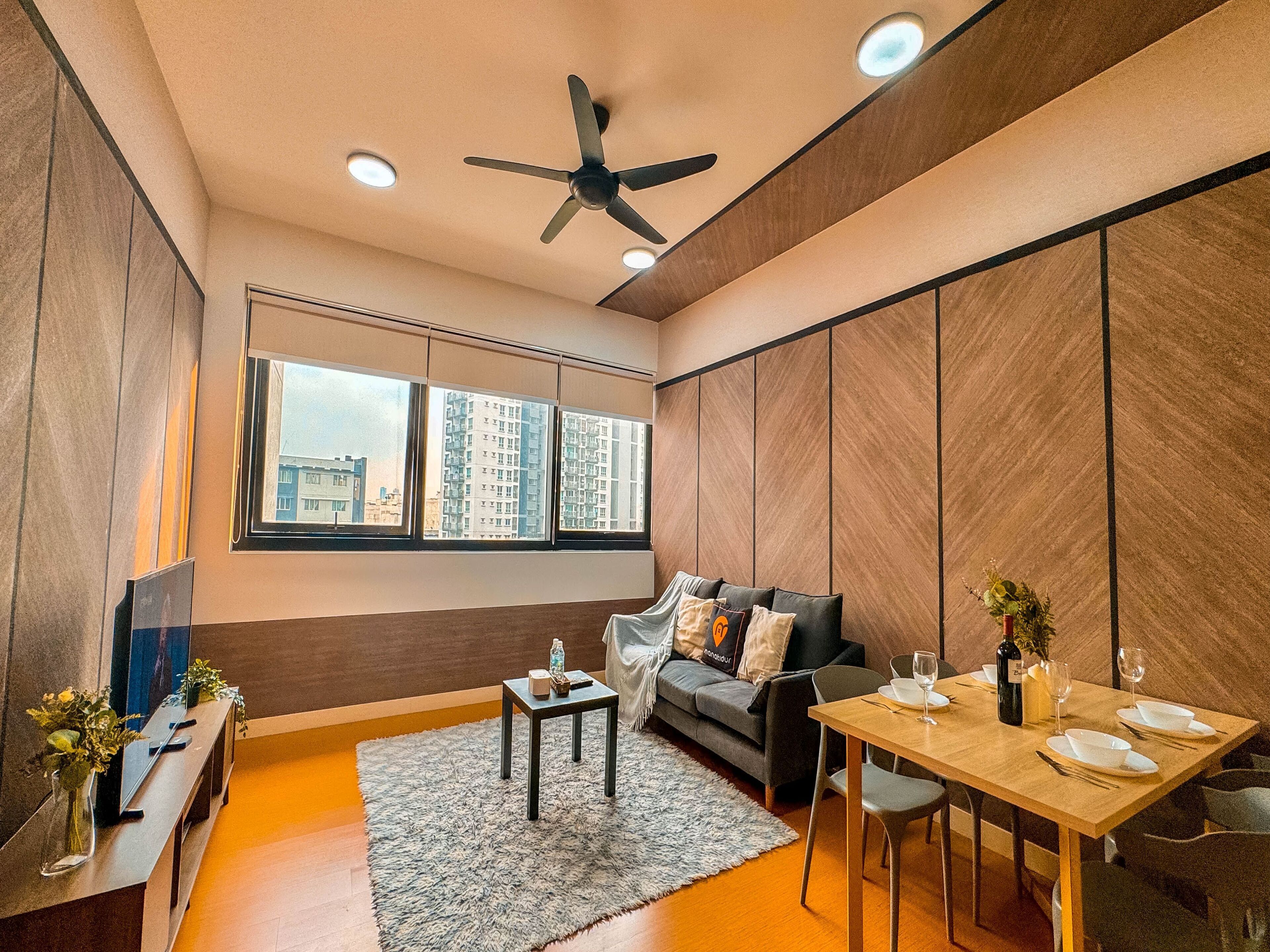 Een moderne woonkamer met een bank, een eettafel gedekt voor twee personen, een plafondventilator en grote ramen met uitzicht over de stad.