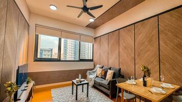 Een moderne woonkamer met een bank, een eettafel gedekt voor twee personen, een plafondventilator en grote ramen met uitzicht over de stad.