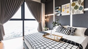 A modern hotel room with a large bed, a view through the window, and artwork on the walls.
