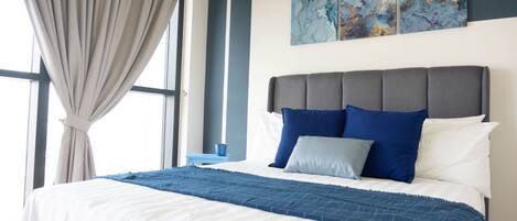 A neatly made bed with a blue and white bedspread, a grey upholstered headboard, and two blue pillows.