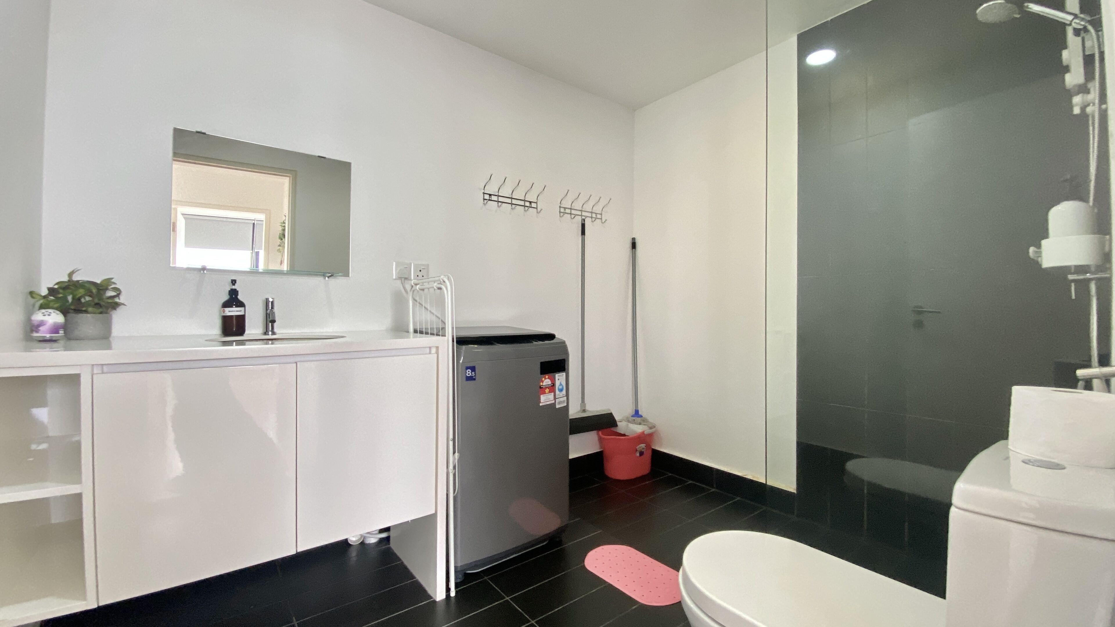 A modern bathroom with a white sink, mirror, and toilet. There is a shower area with a glass door and a handheld showerhead.
