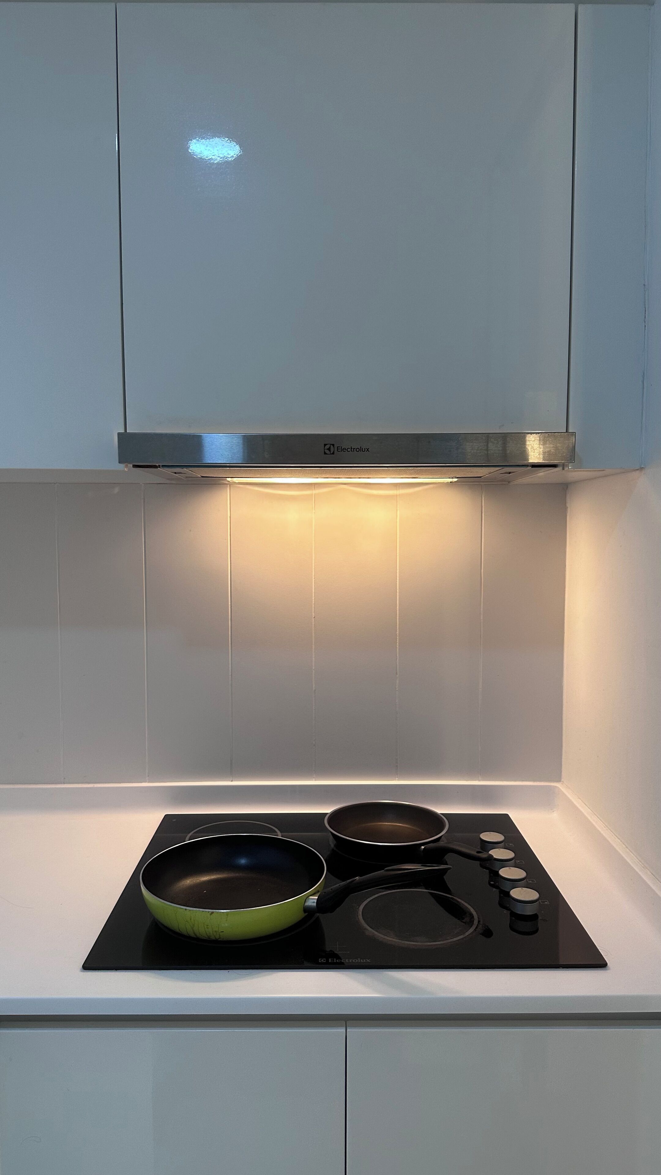 A kitchen with a built-in stove, two frying pans, and a stainless steel range hood.
