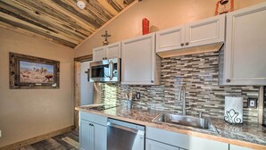 Cozinha com armários brancos, lava-louças de aço inoxidável, micro-ondas e painel de azulejos.