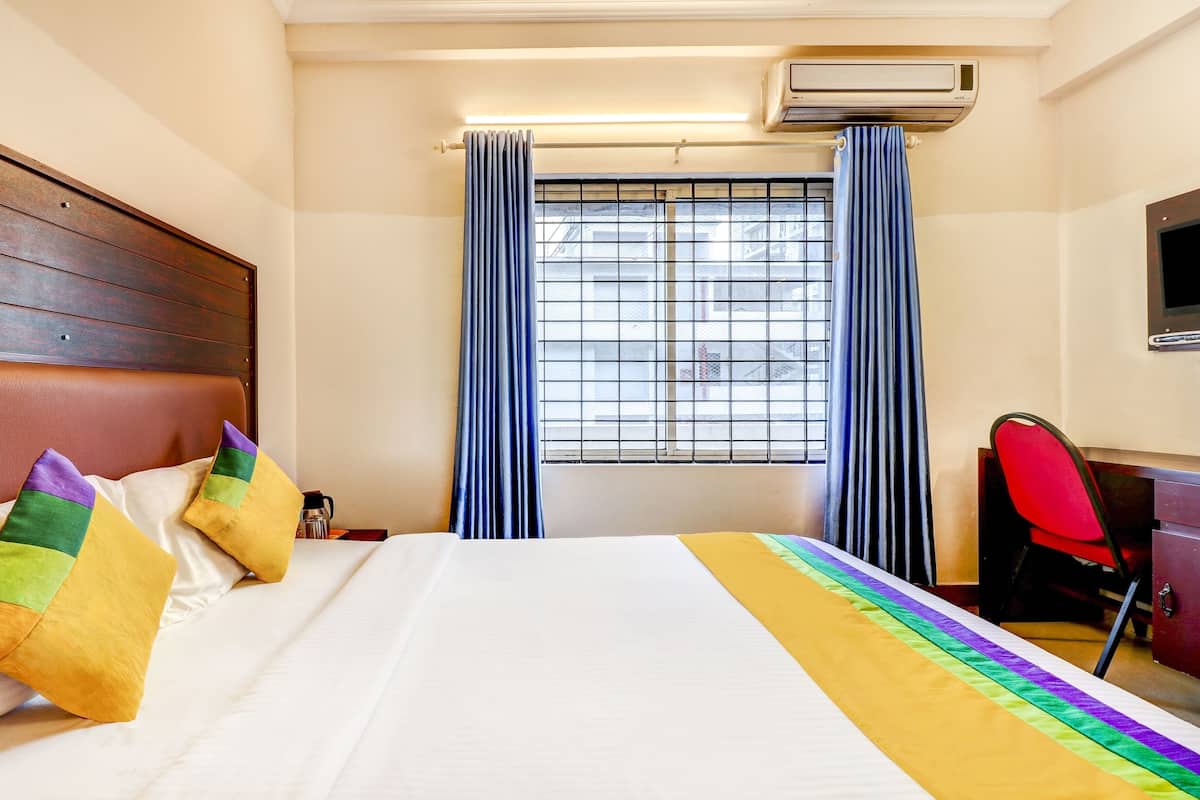 A hotel room with a bed, a desk, an air conditioner, and a window with curtains.