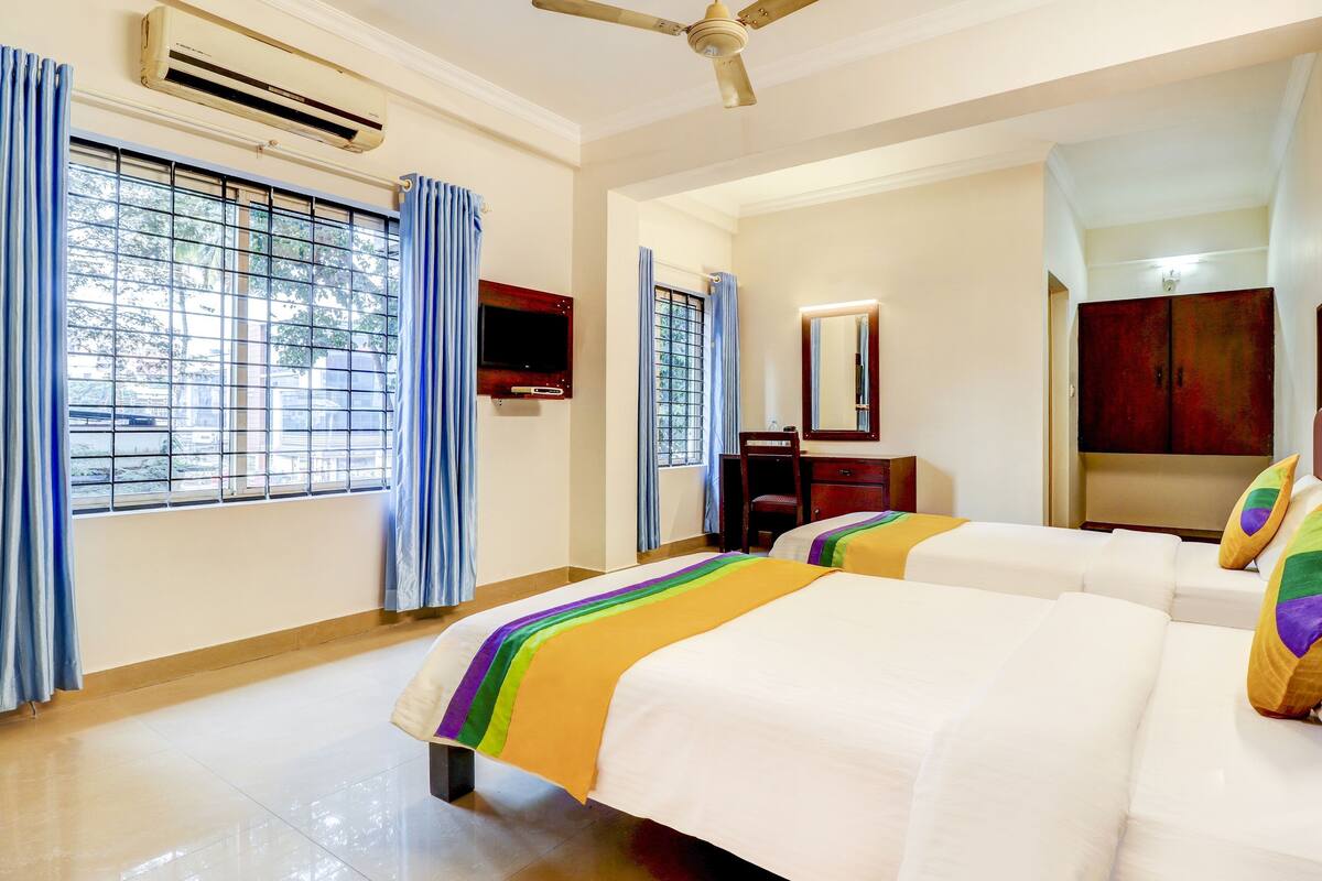 A hotel room with two beds, a ceiling fan, an air conditioning unit, a TV, and a window with a view of the outside.