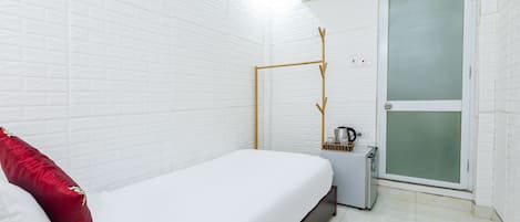 A small, clean room with a single bed, a white wall, a door with frosted glass, and a small table with a kettle.