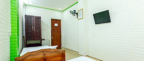 A room with a bed, a wooden wardrobe, a door, a wall-mounted TV, and a green accent wall.