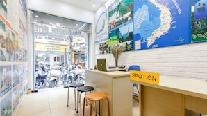 A reception desk with a 'SPOT ON' sign, a map of Vietnam, and a laptop. There are three stools and a vase with flowers. - OYO 604 Queen Hotel (Hanoi)