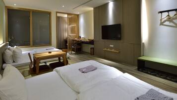 Quarto de hotel com duas camas, uma escrivaninha, televisão e porta de correr para uma varanda.