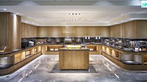 Een modern buffet met een centraal eiland en verschillende bedieningspunten, met een gepolijste marmeren vloer en houten lambrisering.
