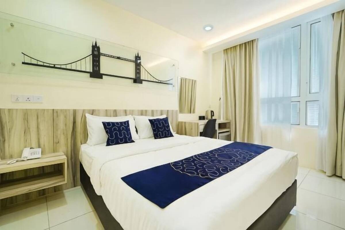 Habitación de hotel con cama, mesita de noche, lámpara y vista a un puente.