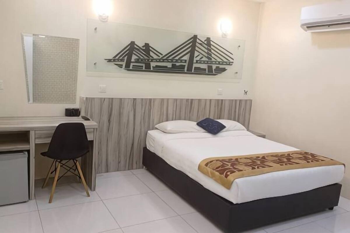Una habitación de hotel con cama, escritorio, silla y aire acondicionado instalado en la pared.