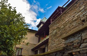 Traditional stone building with a balcony surrounded by lush greenery.
