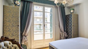Quarto com cama, guarda-roupa, cadeira, janela com cortinas e um candelabro.