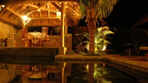 A pool area with a reflection of chairs and a thatched roof structure. - Villa Oasis 1 no 7 (Grand-Baie)