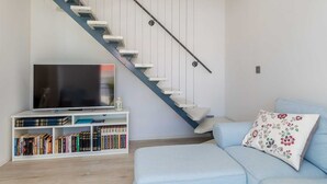 Un saló modern amb una escala, un televisor de pantalla plana, una biblioteca i un sofà blau clar amb un coixí estampat de flors.