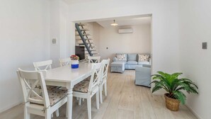 Un espai de viure modern i diàfan amb zona de dinar, escala, sofà i una planta en test.