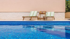 Una piscina d'un blau clar amb dues cadiretes de fusta i una taula petita plena de begudes.