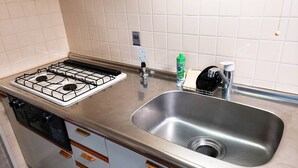 Una cocina con estufa a gas, pileta de acero inoxidable y alacenas de madera.