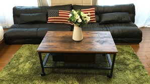 Una sala de estar con un sofá de cuero negro, una mesa de centro de madera con patas de metal y una alfombra de pelo alto color verde.