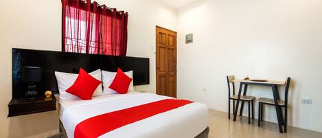 A hotel room with a large bed, a wooden headboard, a desk with two chairs, and a red curtain.