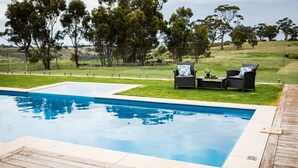 Une piscine dotée d’une terrasse en bois, entourée d’une pelouse et d’arbres.