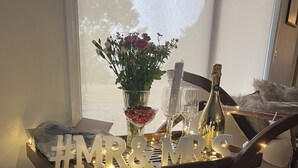 Une table en bois décorée avec des éléments aux motifs « M. et Mme », un vase rempli de fleurs et divers objets en verre.