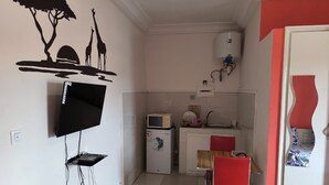 A compact kitchen with a microwave, refrigerator, and sink. A flat-screen TV is mounted on the wall. - Résidence Gian (Libreville)