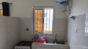 A compact kitchen with a gas stove, a sink, and a window with bars. - Résidence Gian (Libreville)