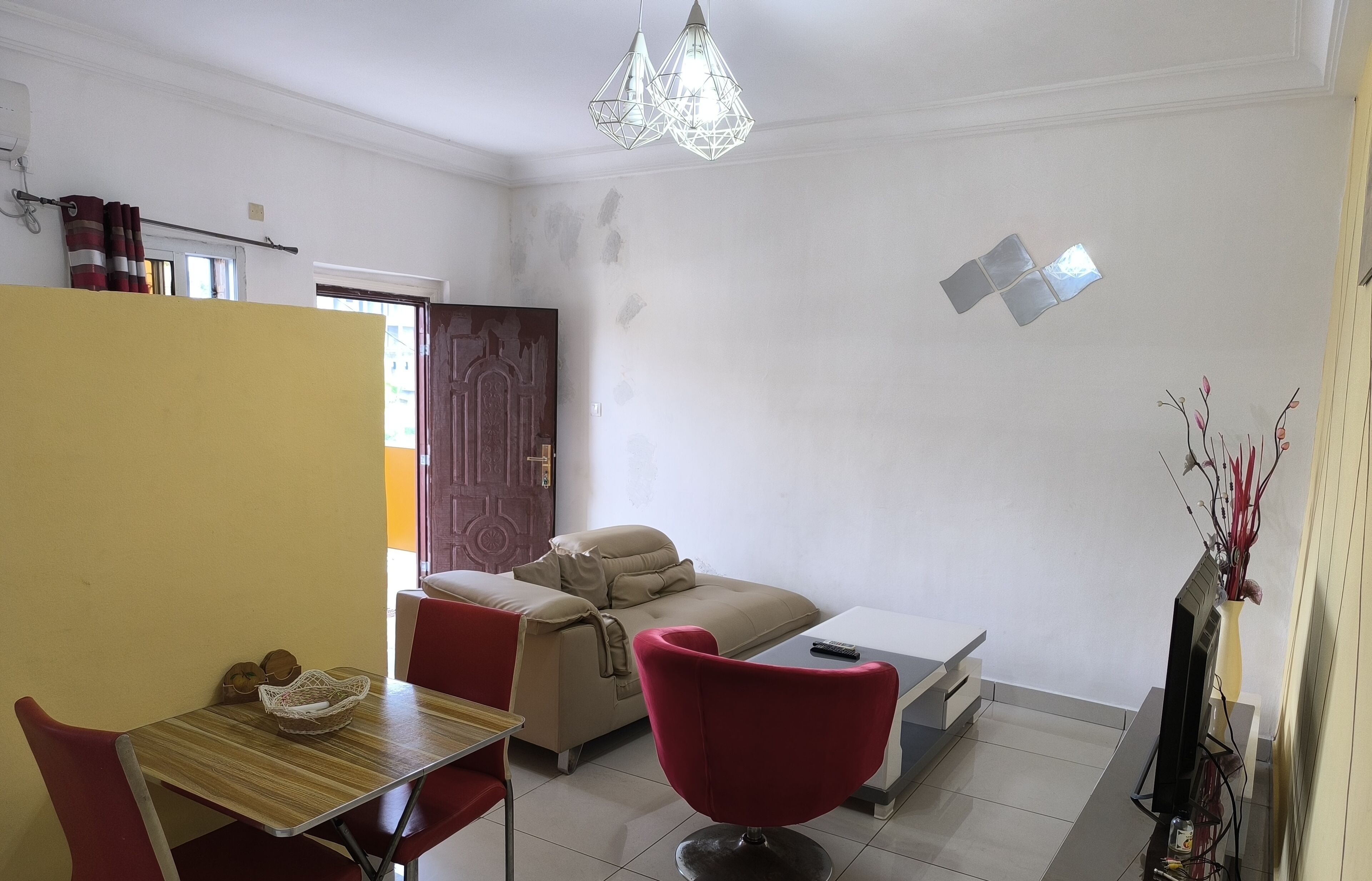 Una sala de estar con sofá, una silla roja, una mesa de comedor con sillas, un televisor y un jarrón decorativo.