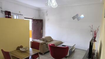 Una sala de estar con sofá, una silla roja, una mesa de comedor con sillas, un televisor y un jarrón decorativo.