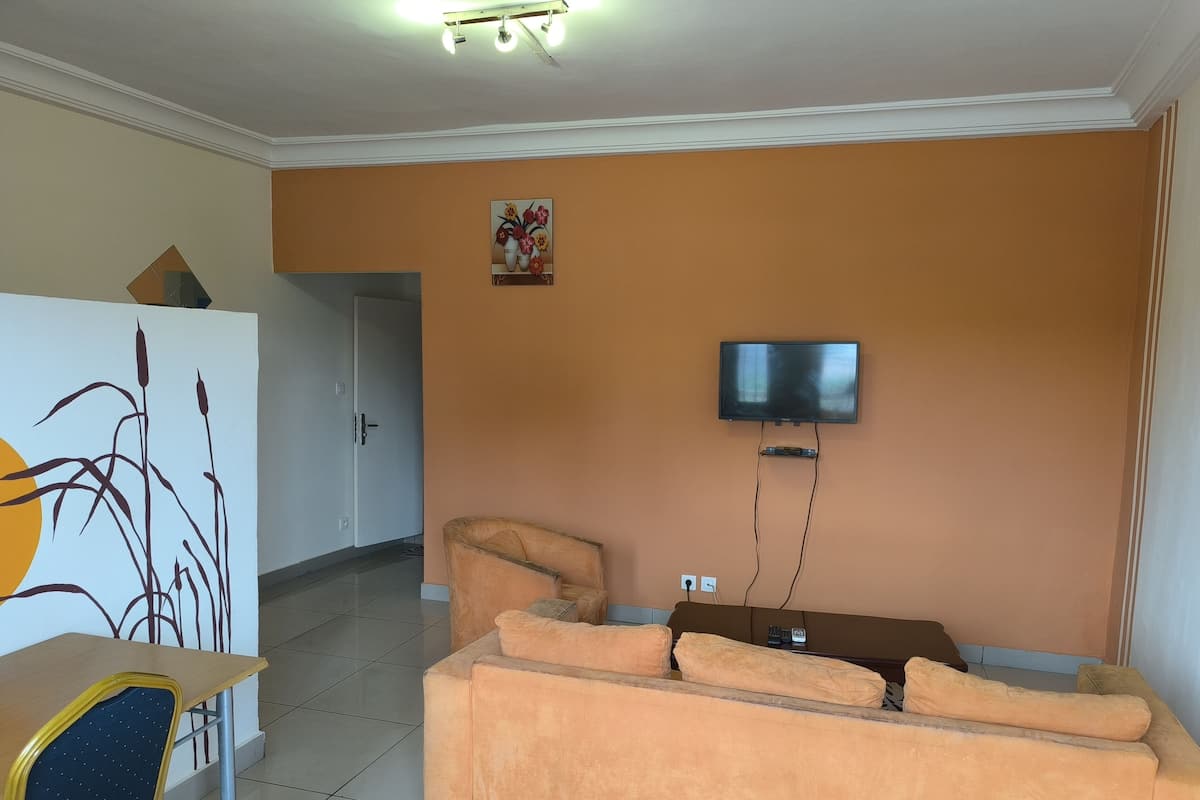 Uma sala de estar com sofá, televisão fixada na parede e um quadro sobre o sofá.